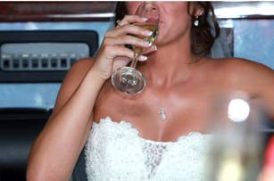 Bride in a strapless lace wedding dress sips from a champagne in a car