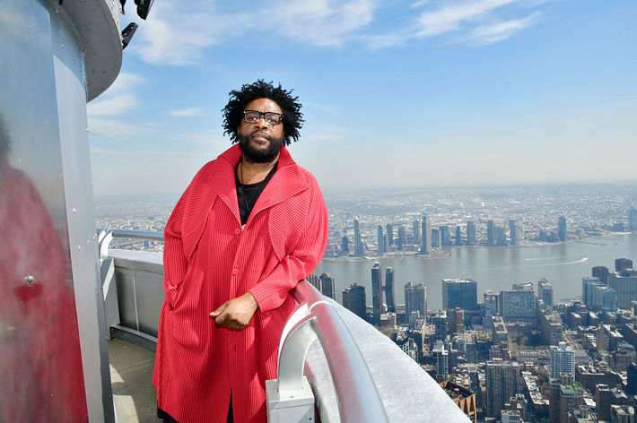 Man standing on a high balcony overlooking a cityscape that includes a river and tall buildings