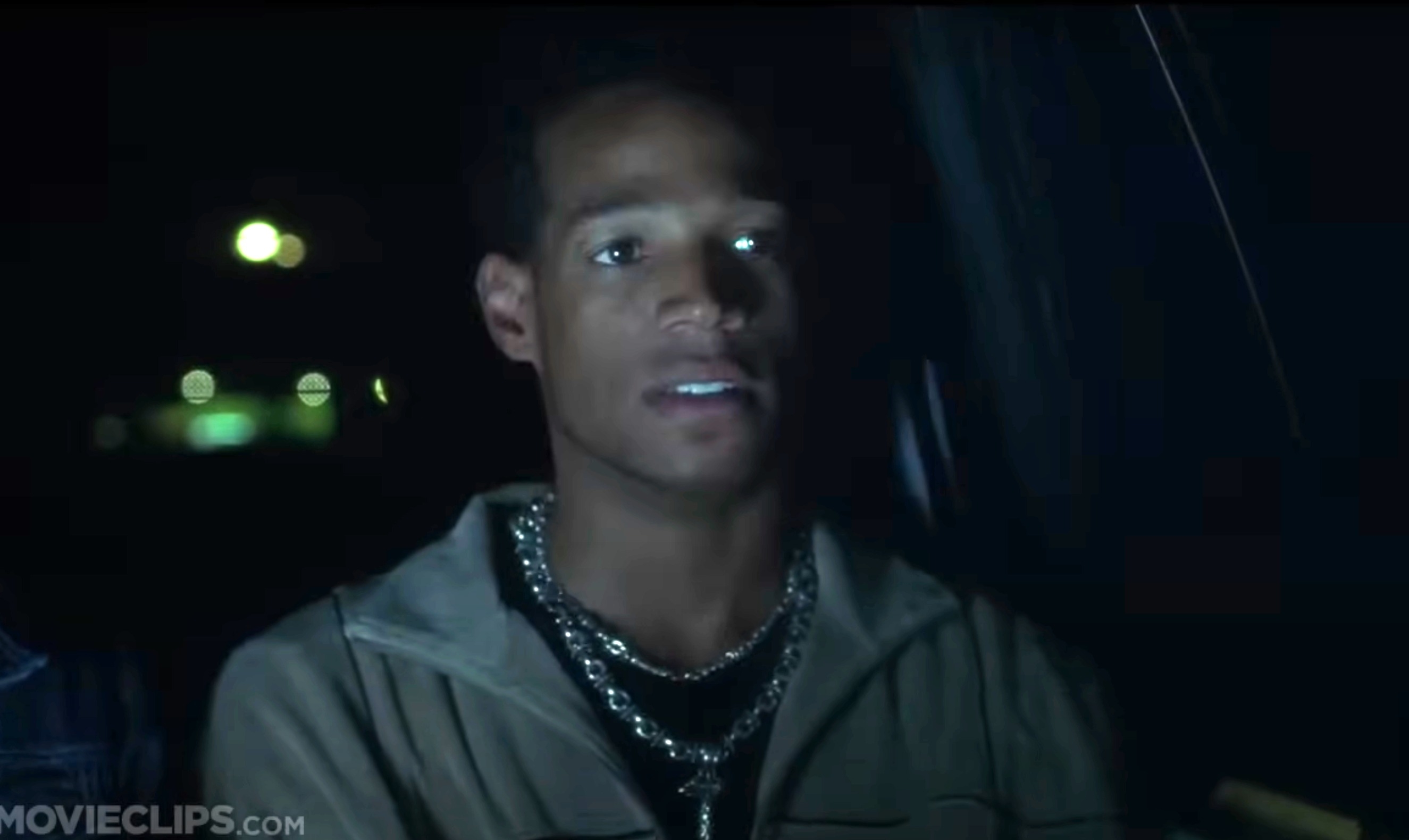 Marlon Wayans appears in a night scene from a movie. He wears a jacket and several silver chains around his neck. The setting is dimly lit