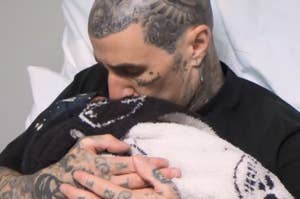 Travis Barker embraces and kisses baby Rocky wrapped in a blanket.