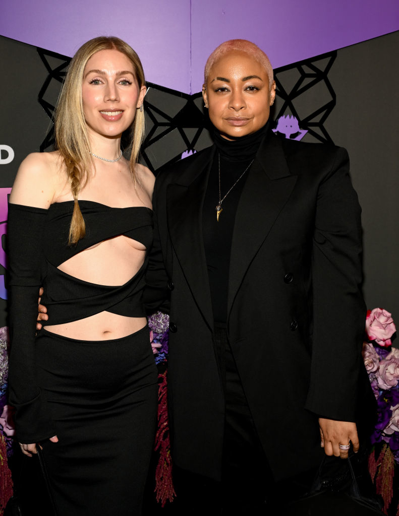 Miranda Maday and Raven-Symoné at a celebrity event, with Raven-Symoné in a black suit and Miranda Maday in an off-shoulder black dress with cutouts