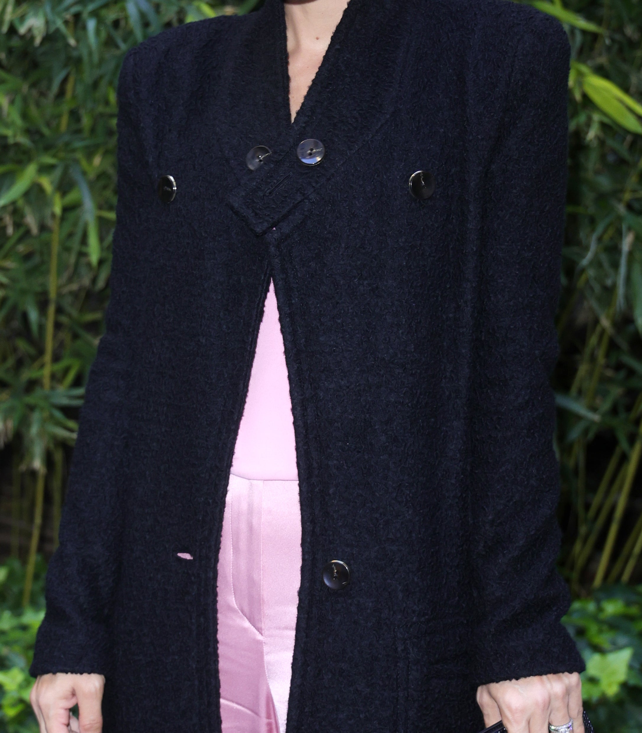 Lily Allen stands outdoors against a leafy backdrop, wearing a long coat