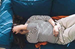 A woman in a striped shirt lies on a sofa, resting with her arm across her forehead