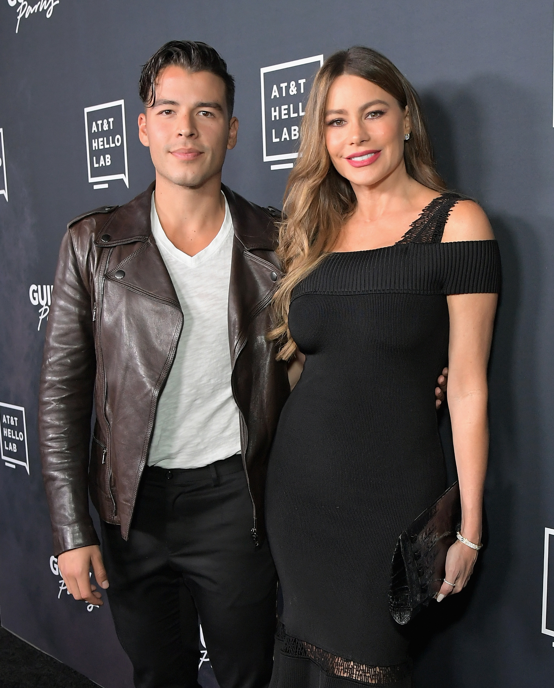 Manolo Vergara wearing a leather jacket, v-neck shirt and dark pants and Sofía Vergara wearing a black strapless dress posing together on the red carpet