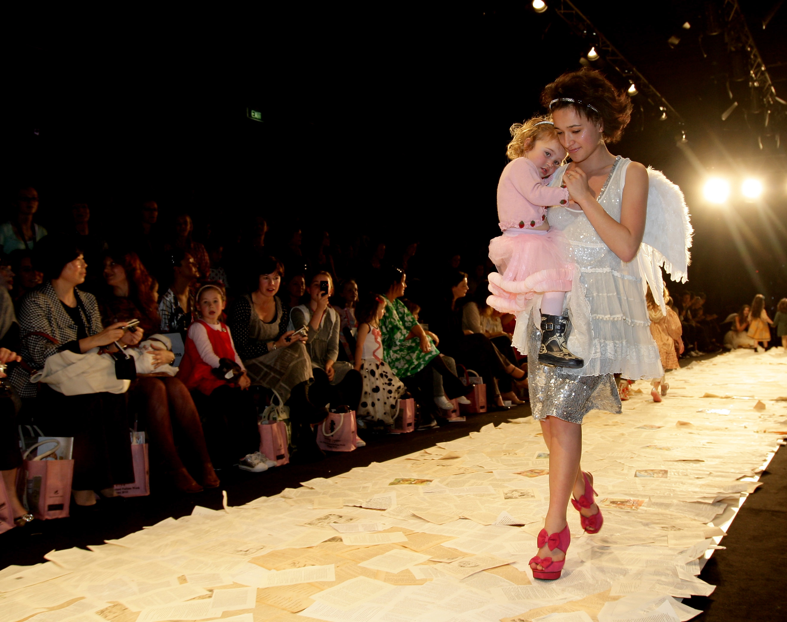 Keisha Castle-Hughes walks down the runway in red heels and a silver/white outfit as she holds her daughter in her arms