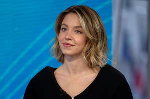 Sydney Sweeney smiles, wearing a casual black top, in a studio setting with a blurred background