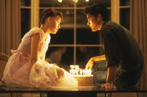 Molly Ringwald and Michael Schoeffling sit across from each other with a cake lit with candles between them in a scene from "Sixteen Candles"