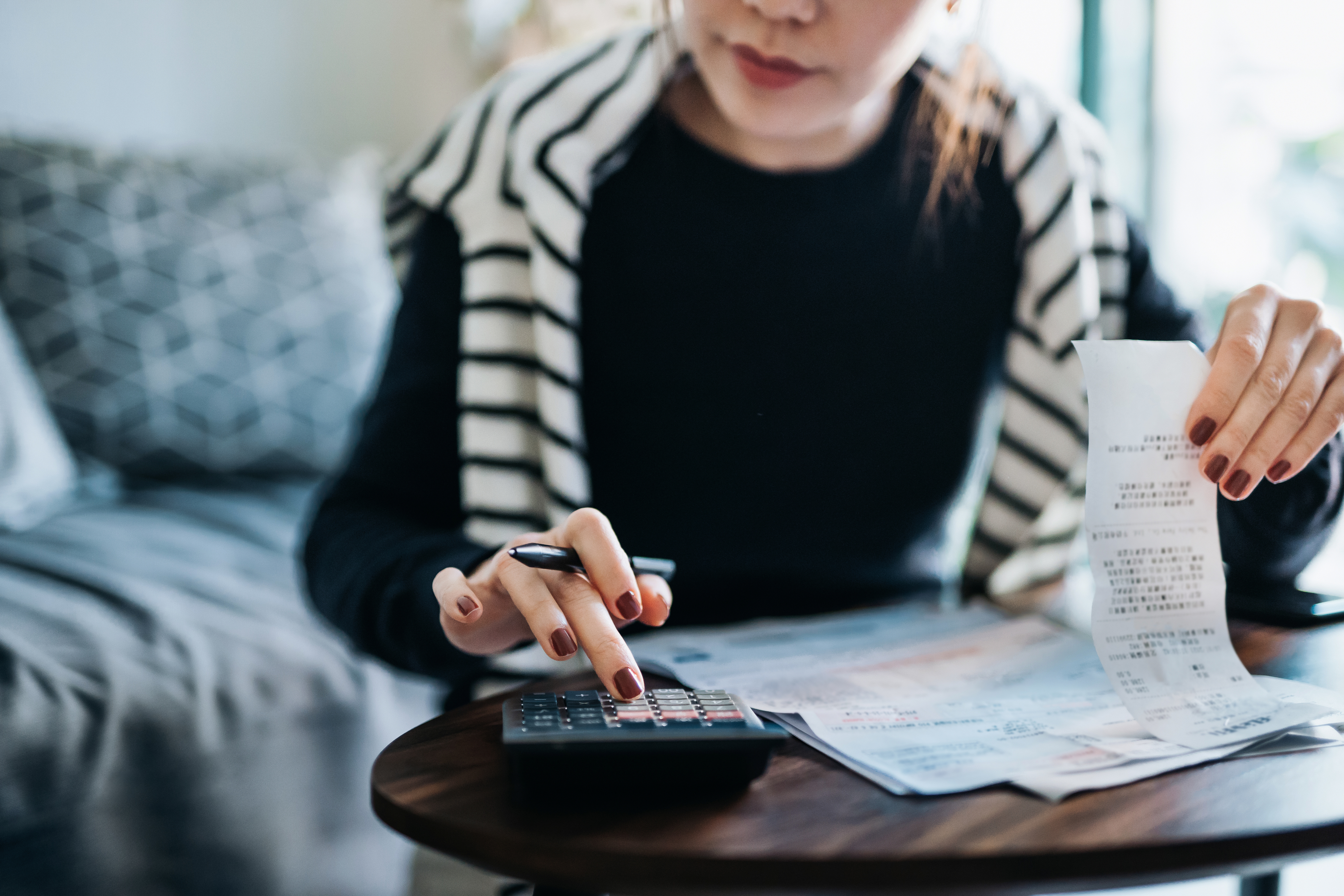 A woman reviewing a receipt while using a calculator, with documents spread out on a table