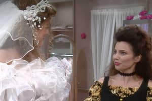 Fran Drescher, wearing a floral top, looks at a woman in a wedding dress adorned with a veil and ruffles in a bridal shop setting