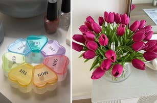 Heart-shaped pill organizer with compartments for each day of the week and a vase of tulips on a table. Nail polish bottles in the background