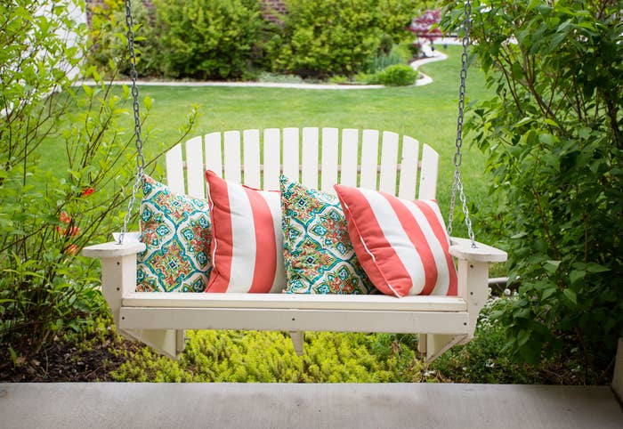 wooden swing bench with patterned pillows, surrounded by greenery in a garden setting