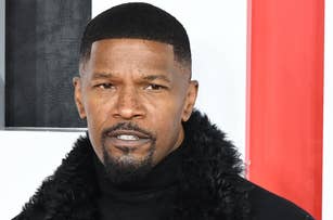 Jamie Foxx on a red carpet, wearing a stylish long black coat with a fur collar over a black turtleneck