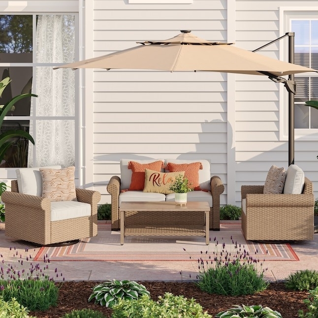 Outdoor patio set with a sofa, two armchairs with white cushions, a table, an umbrella, and various plants surrounding the furniture setup. Decorative pillows on the sofa