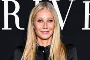 Gwyneth Paltrow smiles while posing against a backdrop at a celebrity event. She is wearing a sleek, black outfit