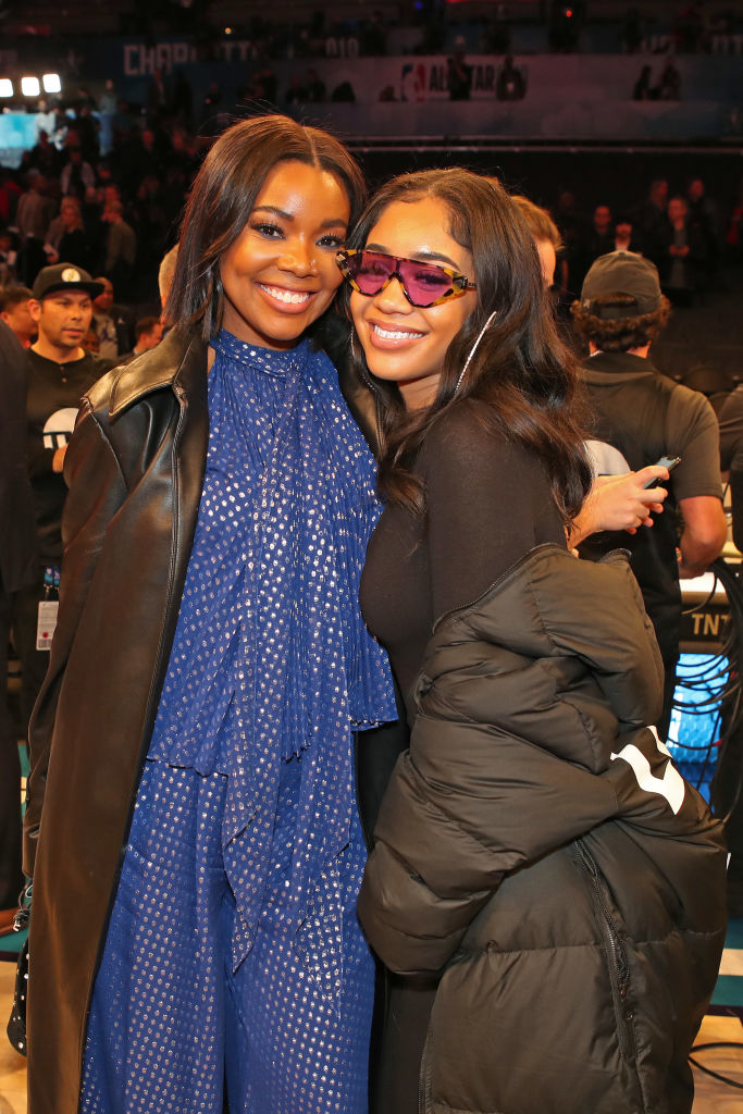Gabrielle Union in a flowy patterned dress and a black leather jacket poses with Saweetie, who wears tinted sunglasses and a puffy jacket, at an event