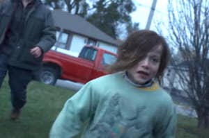 A young child runs distressed with an adult following behind in a suburban neighborhood. The red truck and house are in the background
