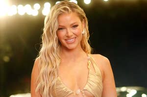 A woman with long, wavy hair smiles while wearing a stylish, low-cut, gold dress at a formal event