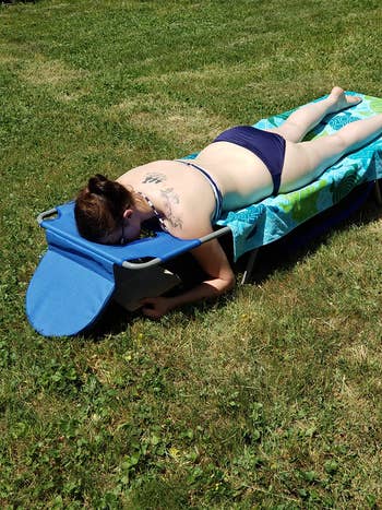 reviewer lying face down on the blue lounge chair with their arms through the holes, reading a book