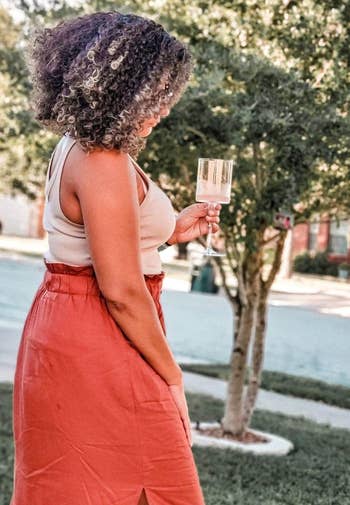 Woman outdoors holding a drink, wearing a sleeveless top and long skirt