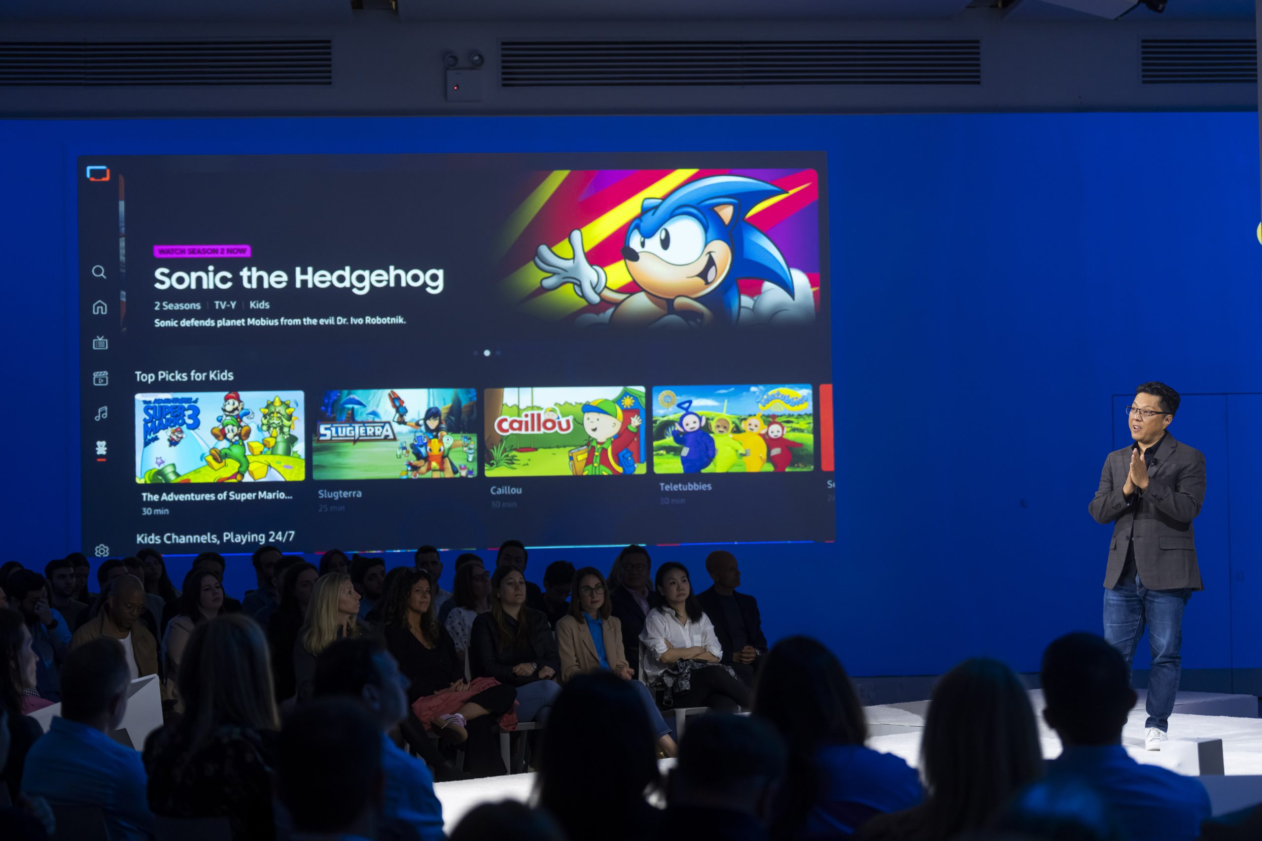 Speaker on stage with display of Samsung Gaming Hub showing Sonic the Hedgehog