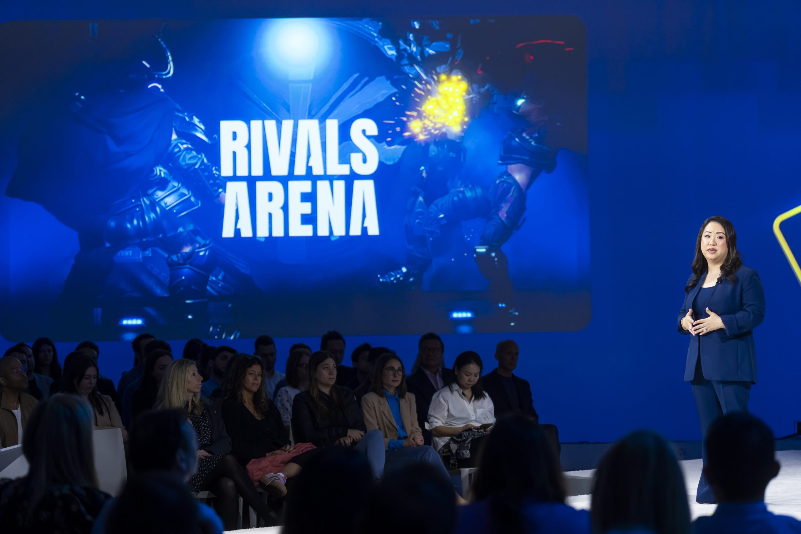 Speaker on stage with display image of Rivals Arena game