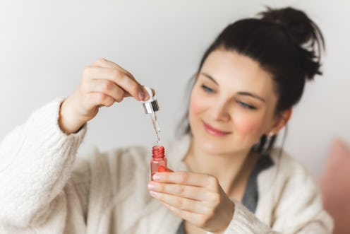 Close up of womans face as she is applying skincare product. Beauty portrait of woman holding bottle...