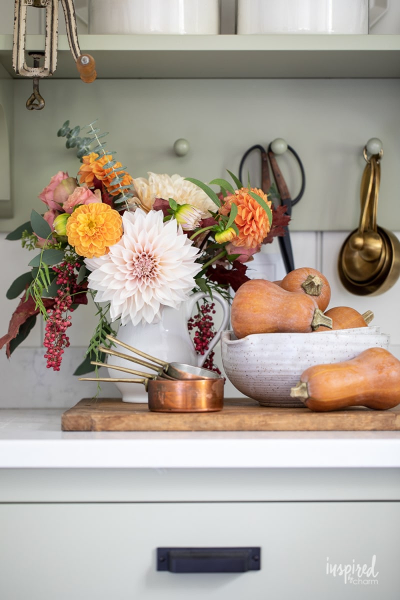 fall flower arrangement with dahilas next to a bowl of squash. 