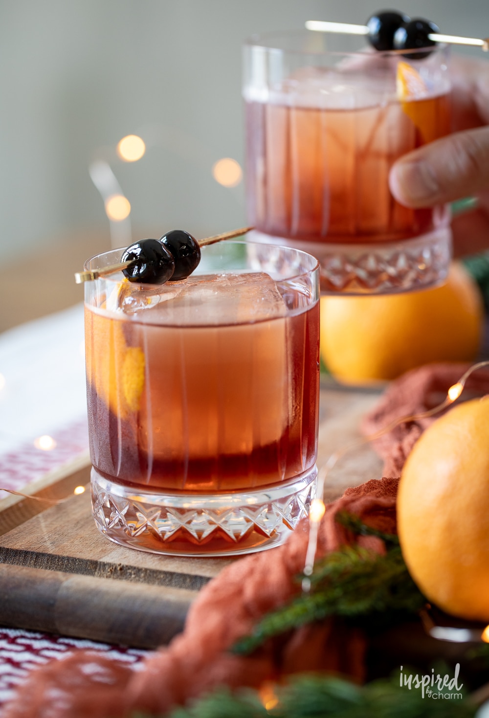 two dolomite old fashioned cocktails with a hand lifting one up. 