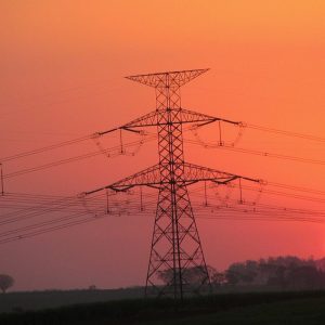 Foto de duas torres de transmissão de energia elétrica com um pôr-do-Sol ao fundo. A matéria explica previsões de dividendos da Taesa (TAEE11) para 2024 e 2025