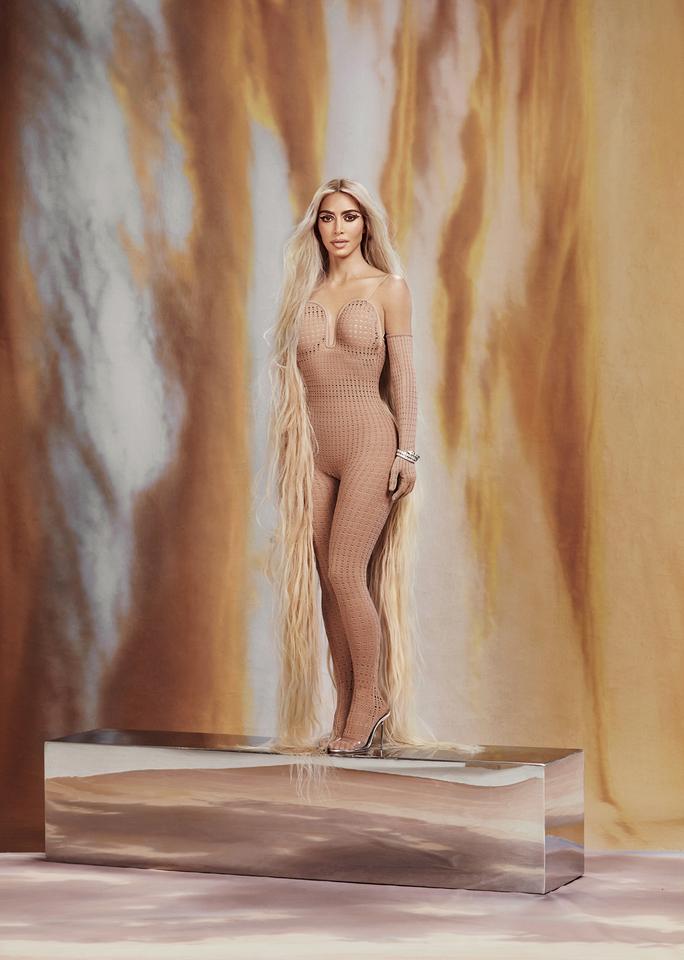 Full-length portrait of Kim Kardashian for Allure Magazine. She’s standing on a rectangular platform wearing a nude, caged bodysuit. Her blonde hair extends down to the floor. 