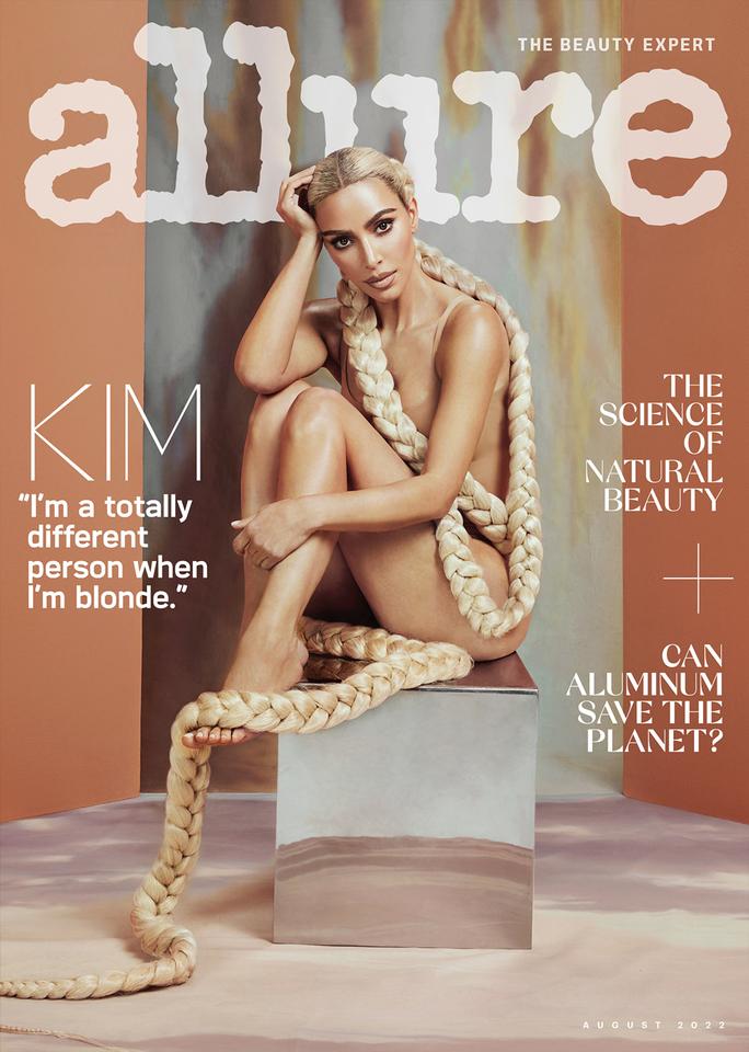 Kim Kardashian on the cover of Allure Magazine, sitting on a box in a nude bodysuit with her knees pulled into her chest. Two 15 foot blonde braids extend from her head to snake around her body.