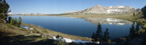 A panoramic view of a lake reflecting a granite mountain.