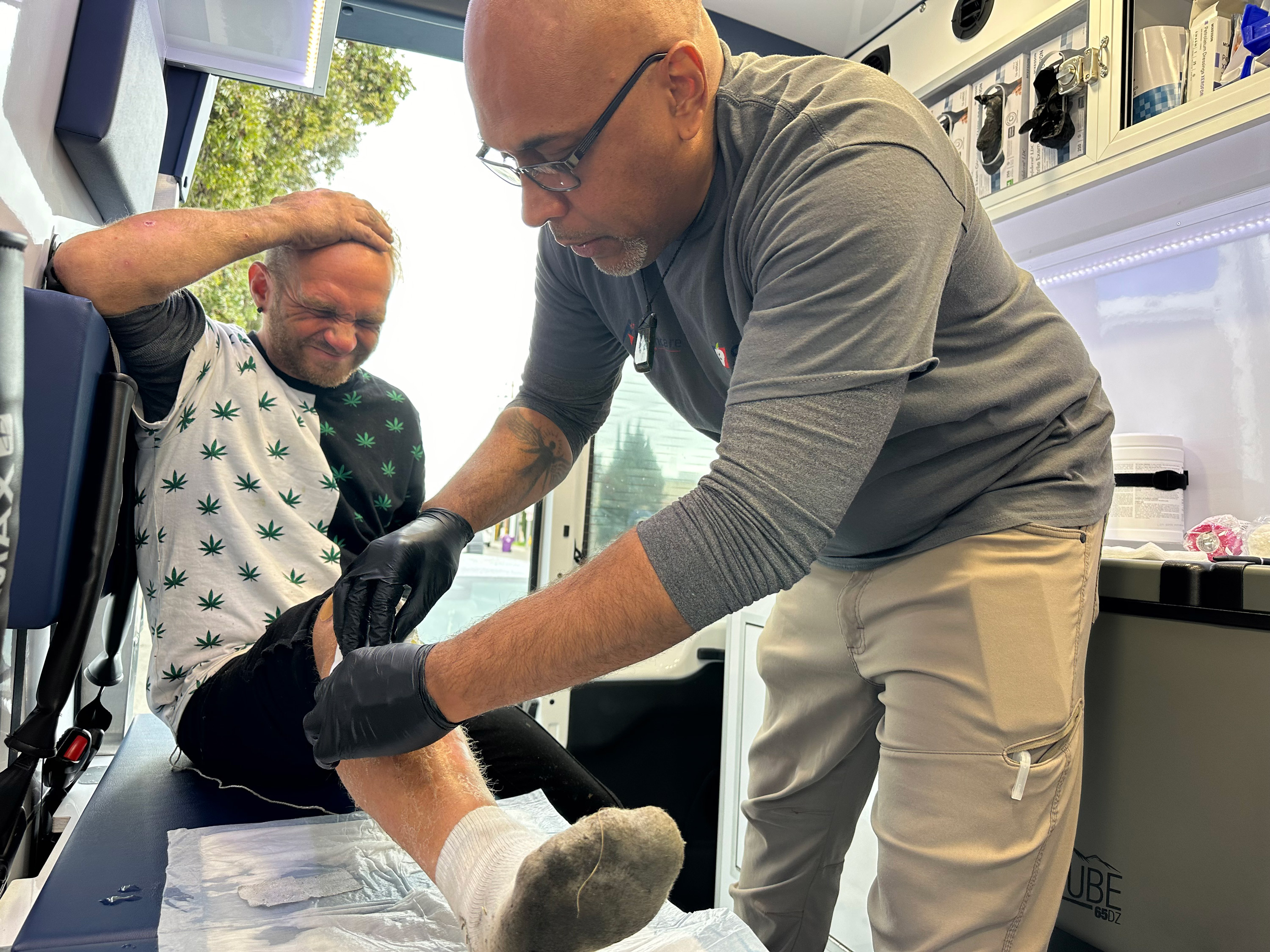 A photo of a medic wrapping a homeless patient's leg with a bandage.