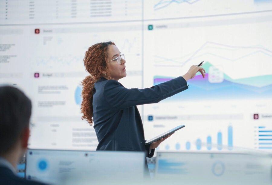 Business woman pointing at a large screen displaying data and charts