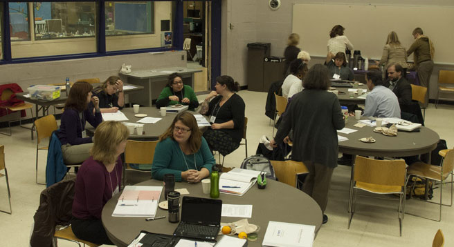 Teachers at a workshop sitting in at tables in groups working on policy.