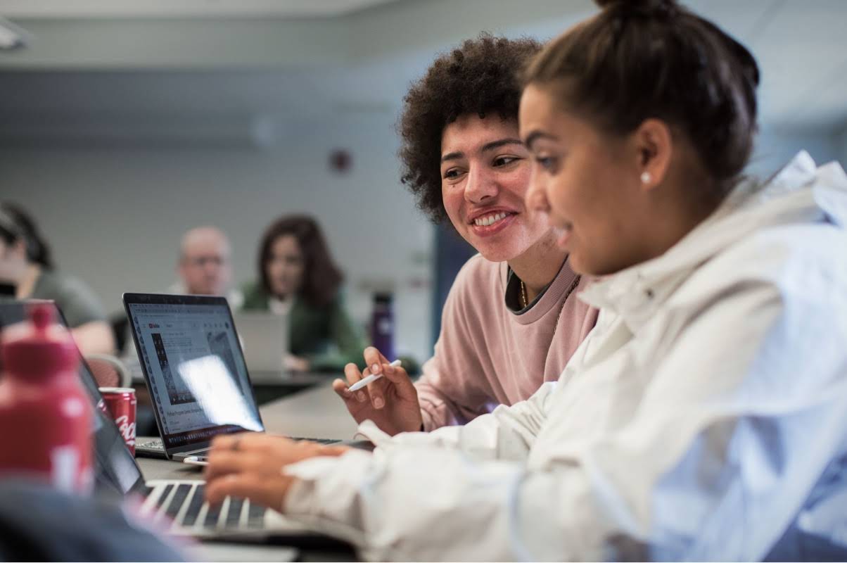 En tenåring skriver på en datamaskin mens en lærer gir råd ved siden av henne