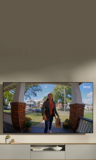 A TV in a living room showing a delivery person standing on a stoop waving to the doorbell camera.