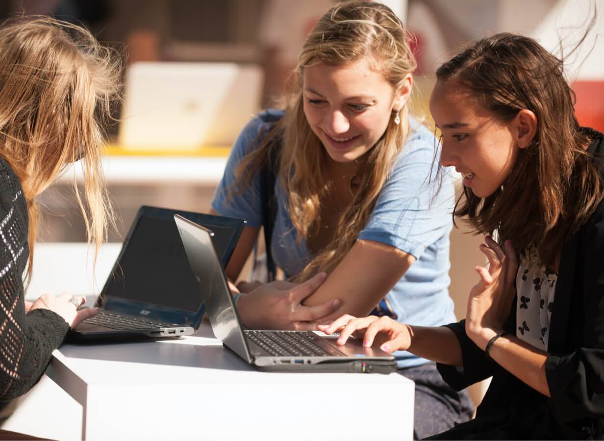 Tre elever sitter ved et bord utendørs og arbeider på hver sin Chromebook