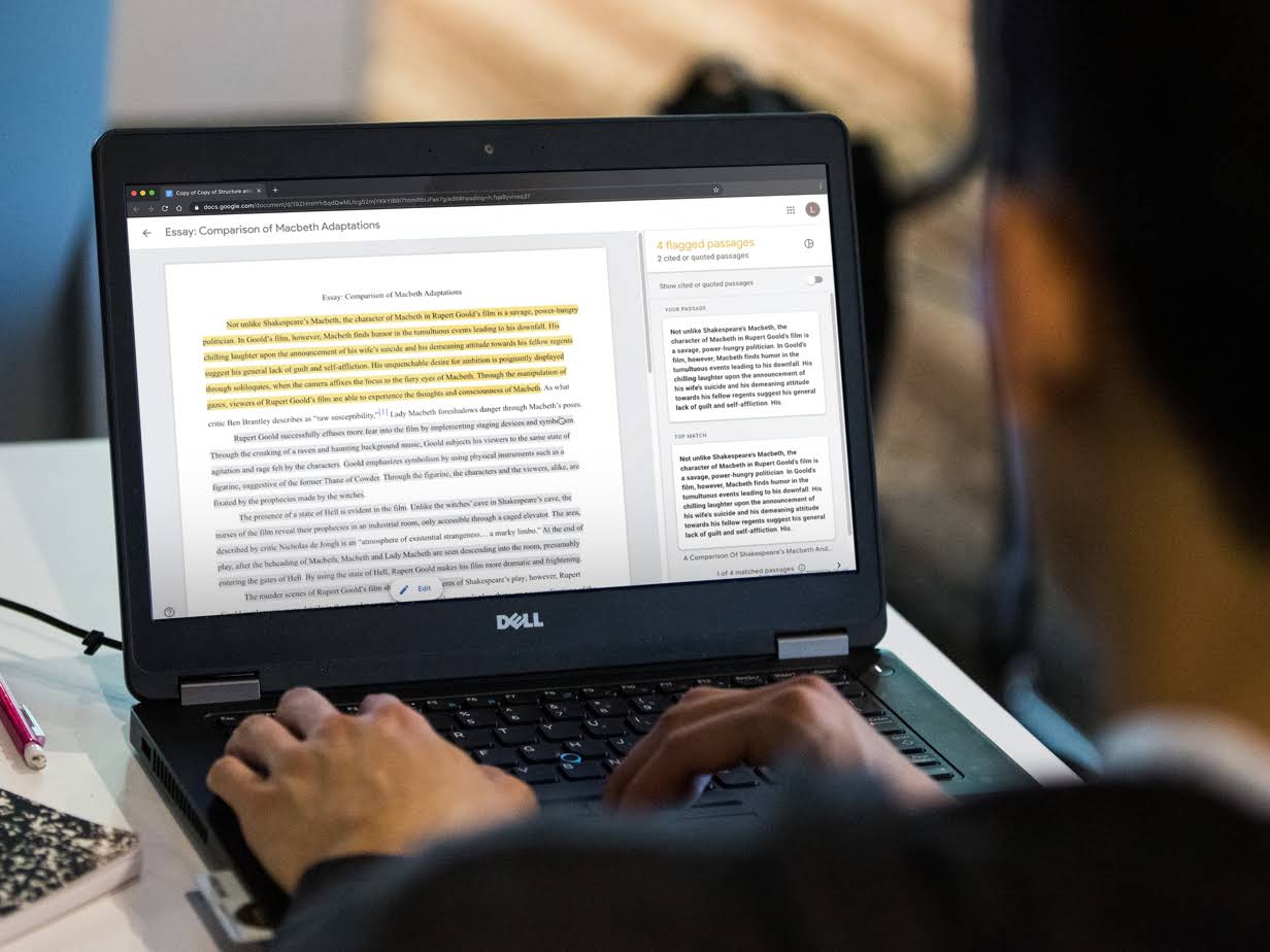 Student hands typing on a Chromebook. On screen, we see a student working on an essay with flagged passages on the right column.