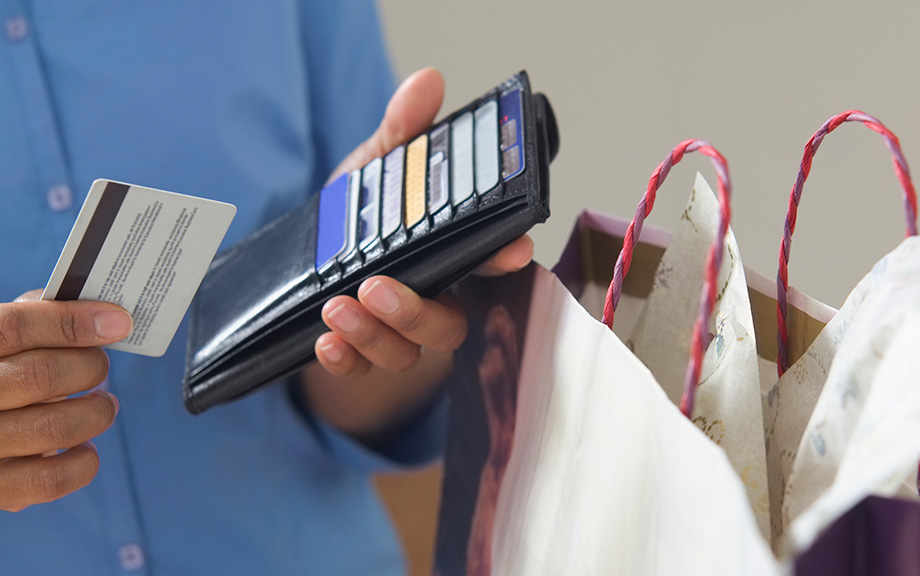 Photo: man holding a wallet in one and a credit card in another with a bag next to him.