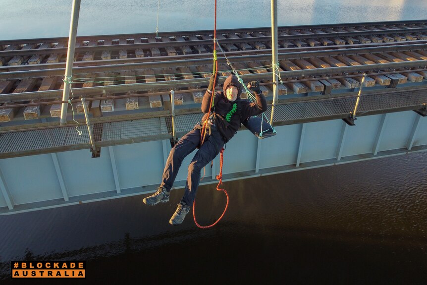 A man hanging from a rope above a train line.