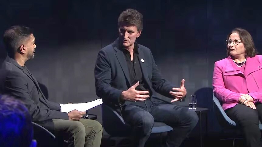 Three people, two men and a woman, sit on a stage having a discussion