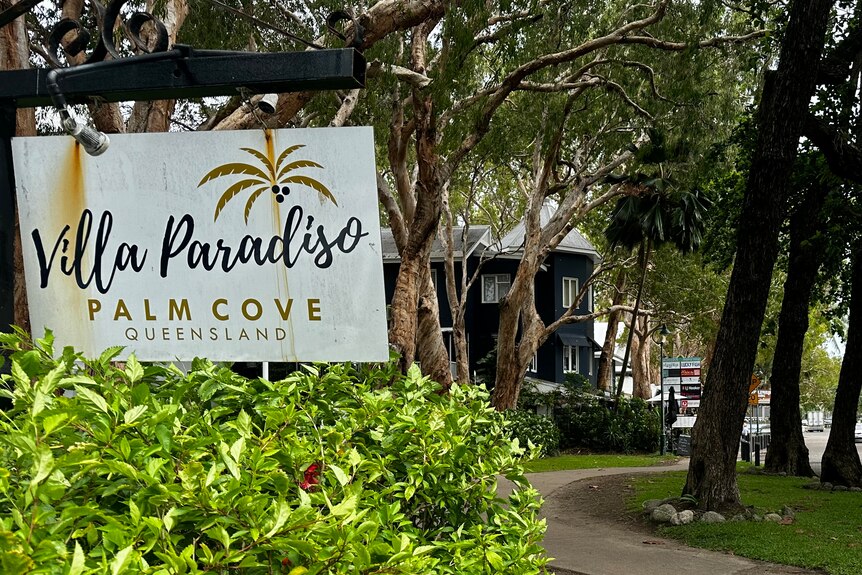 Sign of an apartment building alongside a concrete path winding into the distance and leafy, tropical trees