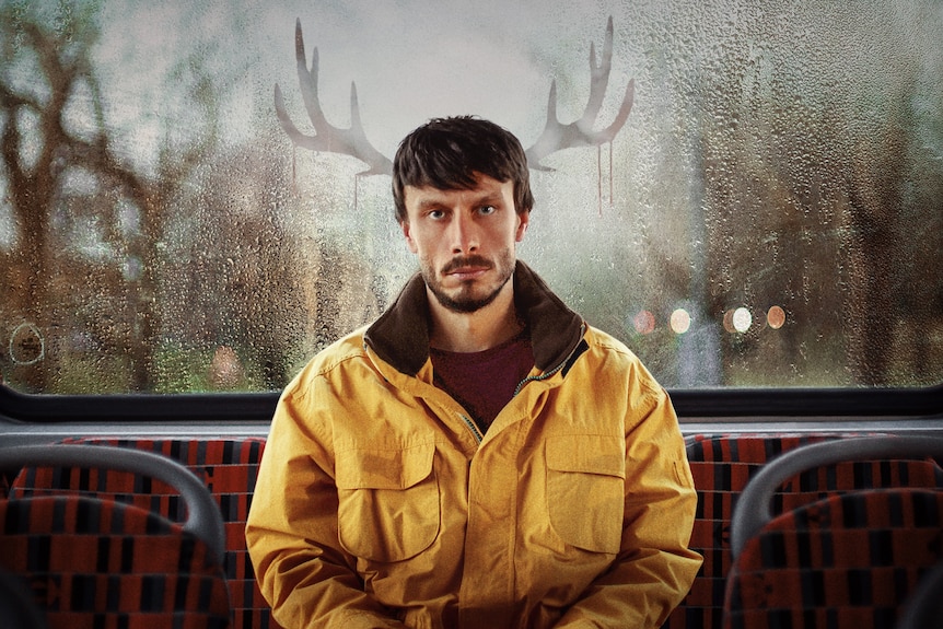 Donny stares into the camera as he sits at the back of a bus wearing a yellow jacket, with antlers photoshopped behind him.