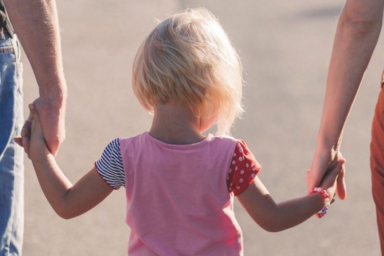 Two adults holding the hand of a young child