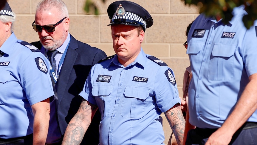 Brent Wyndham in police uniform walking in the middle of a group of police officers. 