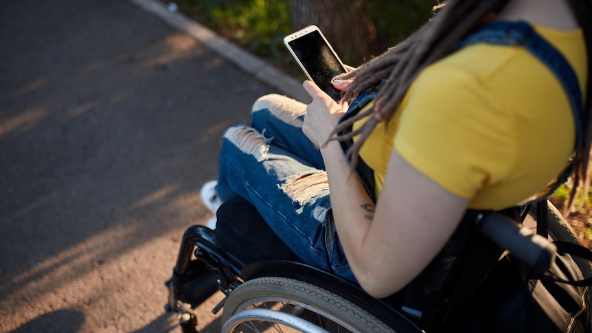 A woman in a wheelchair outdoors using a smartphone