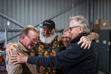 four men hug in a shed