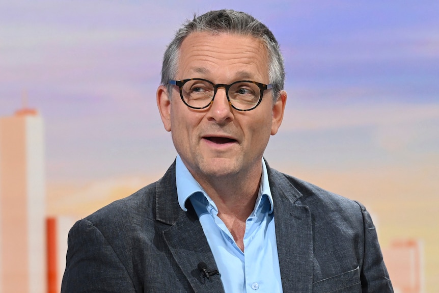 Michael Mosley speaks on a morning talk show wearing a blazer, blue shirt and glasses