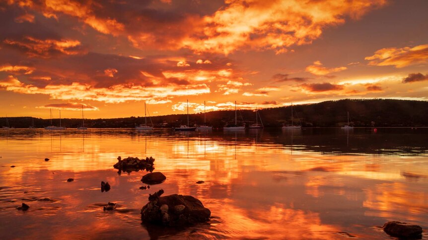 Sunset reflected in still bay waters, with a hill on the horizon.